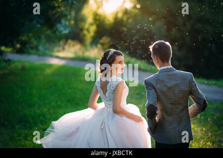 Just Married liebevolle hipster Paar in Brautkleid und Anzug auf der grünen Wiese in einen Wald bei Sonnenuntergang. glückliche Braut und Bräutigam zu Fuß laufen und tanzen im Sommer Wiese. Romantisch heiraten junge Familie Stockfoto