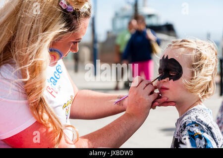 Junge kaukasier Kind, Mädchen, 5-6 Jahre alt, saß in der Sonne Ihr Gesicht mit einer Art Batman Maske durch die blonde Frau gemalt haben. Stockfoto