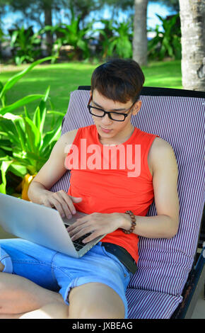 Eine Asiatische junge Mann mit Laptop im Garten in Luxus Resort. Stockfoto