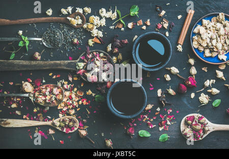 China Schwarzer Tee in schwarzem Steingut Tassen und Holzlöffel mit trockenen Kräuter, Knospen und Blätter über schwarze hölzerne Hintergrund, Ansicht von oben, horizontal Stockfoto