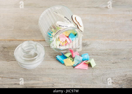 Glas Glas mit handgefertigten Holzmöbeln herzen Dekorationen und Ribbon gefüllt mit bunten Pastell Papier übergreifen. Stockfoto