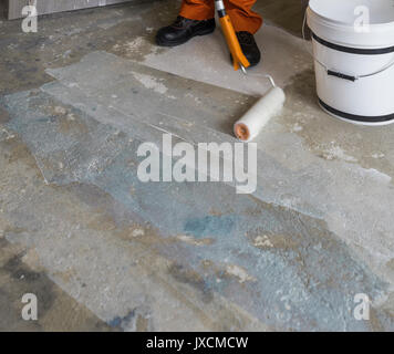 Arbeitnehmer setzt Grundierung mit Walze auf Betonboden. Zimmer von Haus im Bau Stockfoto