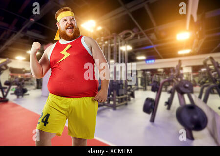 Fett lustige Mann Sieger Lächeln in Sportkleidung in der Turnhalle. Stockfoto