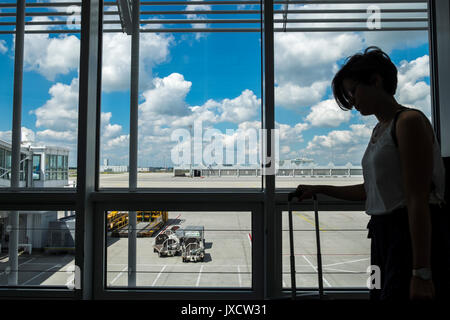 Die Passagiere durch ein Fenster mit Blick auf die Rollbahn am Flughafen München auf dem Weg zu den Abflug-Gates, Bayern, Deutschland Stockfoto