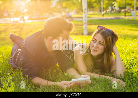 Sonnige Portrait von süssen jungen Paar liegend Entspannen auf dem Gras zusammen hört sich die Musik im Kopfhörer auf dem Smartphone, Sommer Tag Stockfoto