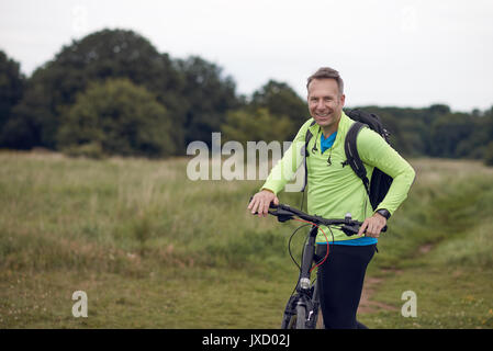 Lächelnd reifer Mann tragen Sportswear auf Radtour durch Wiese Stockfoto