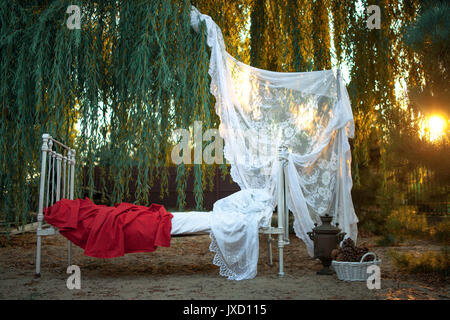 Weiß Bett mit Bettzeug und Lacy Baldachin auf Sand in der Nähe von Tree auf den Sonnenuntergang. Konzept der Ruhe, Entspannung und Gelassenheit. Stockfoto