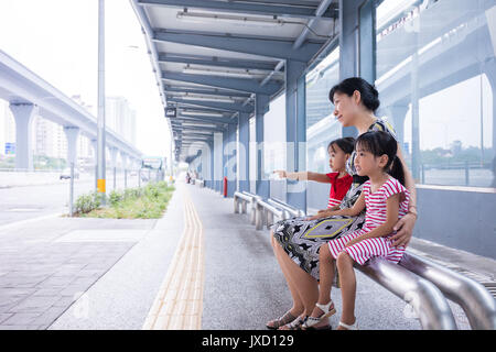 Asiatische chinesische Mutter und Töchter warten auf einen Bus an der Haltestelle Stockfoto