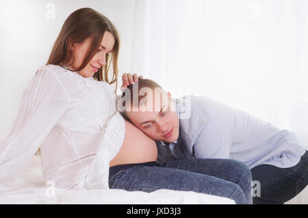 Schöner Mann ist das Hören von Bauch seine schöne schwangere Frau. Happy Family Konzept Stockfoto