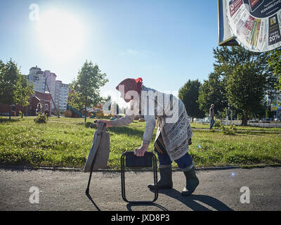 Arme alte Frau, die zu Fuß mit einem verbogenen zurück um die Stadt herum und betteln. In Belarus gefilmt. Stockfoto