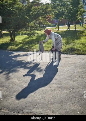 Arme alte Frau, die zu Fuß mit einem verbogenen zurück um die Stadt herum und betteln. In Belarus gefilmt. Stockfoto