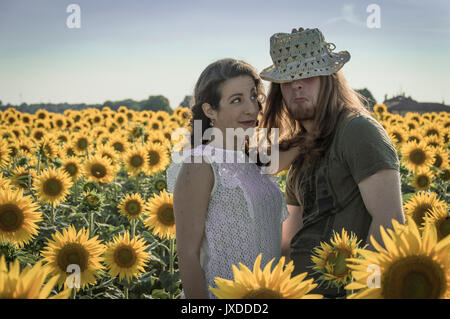 Spontane attraktive junge Brautpaar teilen einen guten Witz lacht schallend und umarmen einander im Freien in einem Sonnenblumenfeld Stockfoto