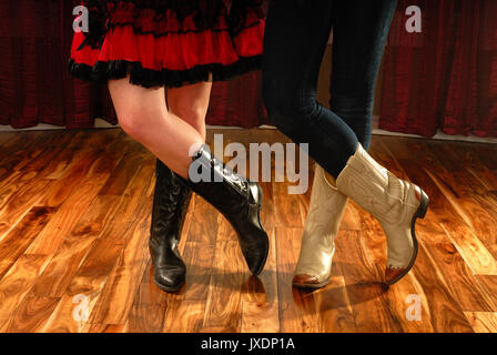 Weibliche Beine in Cowboystiefeln in einem Line Dance Schritt auf Parkett Stockfoto