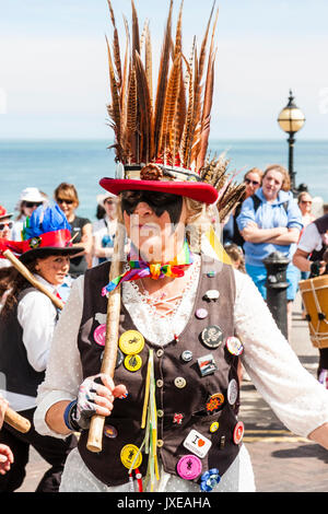 England, Broadstairs folk Woche. Dead Horse und die broomdashers Morris Seite. Frau aus dem Broomdashers tanzen während Sie Holz- personal. Tragen Motorhaube mit Federn auf. Menschen und Meer im Hintergrund. Stockfoto