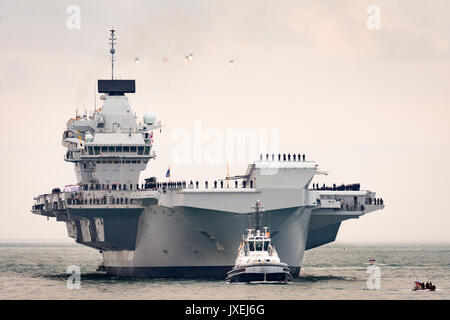 Portsmouth, Großbritannien. 16 Aug, 2017. Schlepper, die HMS Queen Elizabeth in Portsmouth Harbour mit ihrem Hubschrauber escort oben Credit: Vernon Nash/Alamy leben Nachrichten Stockfoto