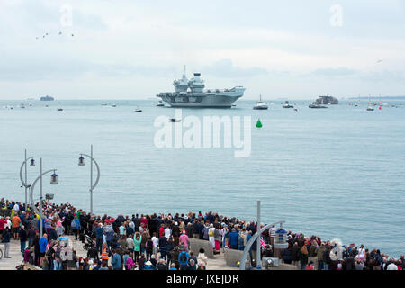 Portsmouth, Großbritannien. 16 Aug, 2017. HMS Queen Elizabeth segeln in Portsmouth Es ist Heimathafen für die erste Zeit. Große Menschenmenge auf dem Meer Wand einladende neueste und größte Kriegsschiff in Großbritannien. Flug der Hubschrauber von der Begleitung des Flugzeugträger Overhead. Quelle: David Robinson/Alamy leben Nachrichten Stockfoto