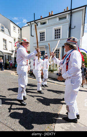 Traditionelle englische Morris Men von Hartley Morris Dancers außerhalb der Stadt Straße an der jährlichen Broadstairs Folk Woche. Tanzen in zwei Reihen tragen weiße Hosen und Hemden mit Stroh Hüte, holding Holzpfähle. Stockfoto