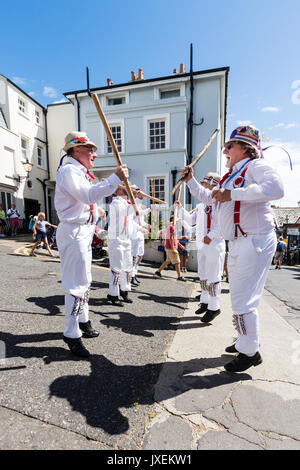 Traditionelle englische Morris Men von Hartley Morris Dancers außerhalb der Stadt Straße an der jährlichen Broadstairs Folk Woche. Tanzen in zwei Reihen tragen weiße Hosen und Hemden mit Stroh Hüte, holding Holzpfähle. Stockfoto