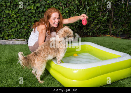 Schöne rothaarige Frau spielt mit ihrem Hund in den Garten Stockfoto