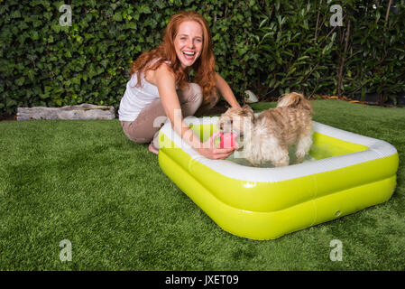 Schöne rothaarige Frau spielt mit ihrem Hund in den Garten Stockfoto