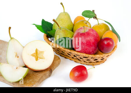 Obst Zusammensetzung - eine hölzerne Weidenkorb mit ganzen reife Früchte - Birnen, Pflaumen, Aprikosen und Äpfeln, in der Nähe der in Scheiben geschnittenen Apfel und Birne auf Holzbrett Stockfoto