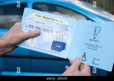 Woman's Hände halten ein Blue Badge Parkscheibe in Großbritannien für behinderte Fahrer. Stockfoto