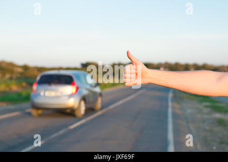 Reise, Reisen, Geste und Personen Konzept - Mann per Anhalter fahren und anhalten Auto mit Daumen nach oben Geste auf Landschaft Stockfoto