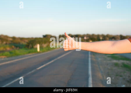 Reise, Reisen, Geste und Personen Konzept - Mann per Anhalter fahren und anhalten Auto mit Daumen nach oben Geste auf Landschaft Stockfoto