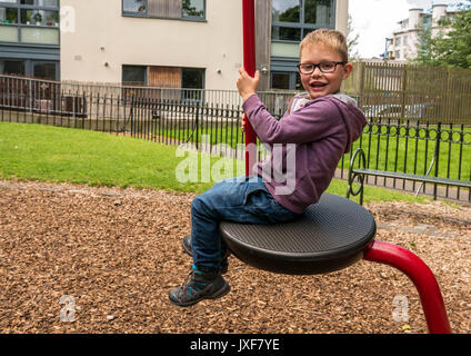 Nahaufnahme von Glücklich lächelnde Junge mit Brille auf der Schaukel in Play Park in Leith, Edinburgh, Schottland, Großbritannien. Stockfoto