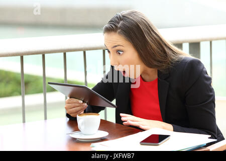 Erstaunt Executive erhalten gute Nachrichten in einen Tablet-PC in einem Café sitzen Stockfoto