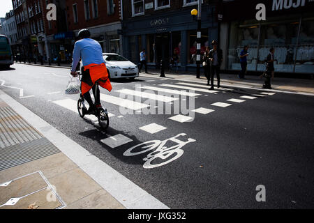 Ein Londoner Arbeiter Radfahren über Zebrastreifen während Auto wartet für Fußgänger auf der Kings Road, Sloane Square, London. Stockfoto