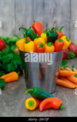 In der Nähe der bunten mini Gemüsepaprika in einem vintage Korb über eine hölzerne Hintergrund Stockfoto