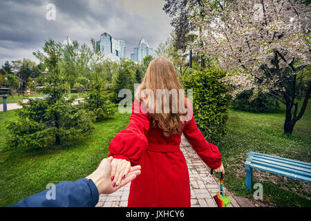 Frau im roten Mantel und Schirm halten sie ihre Freundin und führt zu der Stadtpark mit Cherry Blossom und bedecktem Himmel Stockfoto