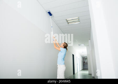 Junge Frau Reinigung der Decke mit Mop auf dem Flur des Gebäudes Stockfoto