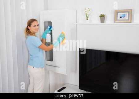 Junge lächelnde Frau Reinigung Möbel mit Reinigung Produkt zu Hause Stockfoto