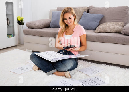 Junge lächelnde Frau sitzt auf dem Teppich Berechnung Rechnung mit Rechner zu Hause Stockfoto