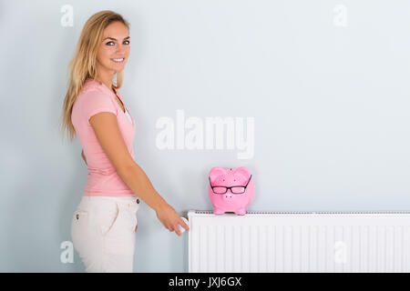 Lächelnde junge Frau einstellen Thermostat Heizung reduzieren, um Geld zu sparen auf der Stromrechnung Stockfoto