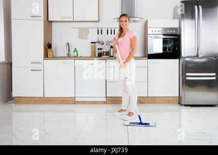 Portrait der junge lächelnde Reinigung Frau mit Mop in der Küche zu Hause stehend Stockfoto