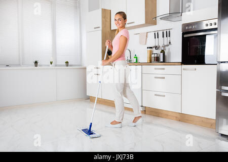 Lächelnde Frau mit Mop Reinigung Reinigung Fußboden in der Küche zu Hause Stockfoto