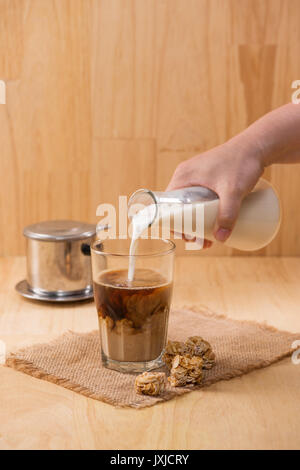 Gießen Milch im Glas Kaffee auf einem Holztisch. Stockfoto