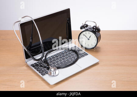 Schrägansicht von schwarz und silber Metall Stethoskop auf Laptop und Wecker auf Holz- Oberfläche Stockfoto