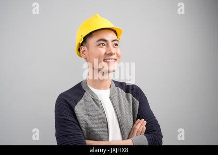 Portrait von lächelnden asiatischer Mann tragen, hardhat beim Stehen Arme auf grauem Hintergrund gekreuzt Stockfoto