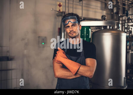 Portrait des jungen Mannes in schützende Arbeitskleidung in der Brauerei. Brauerei Brauerei Anlage mit industriellen Anlagen im Hintergrund arbeiten. Stockfoto