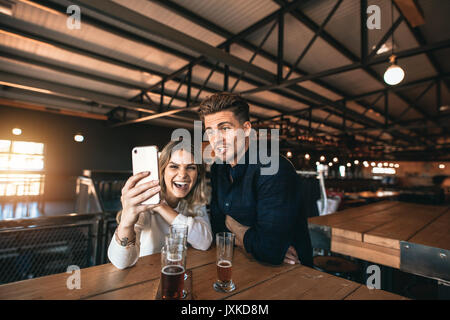 Glückliches Paar ein selfie mit einem Smartphone in eine Bar. Lächelnd Mann und Frau an Brewery Bar sitzen mit Bier auf dem Tisch, die self portrait mit Stockfoto