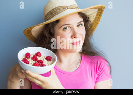 Lächelnde Frau halten gesund und natürlich Frühstück, Haferflocken und Himbeeren in eine Schüssel geben Stockfoto