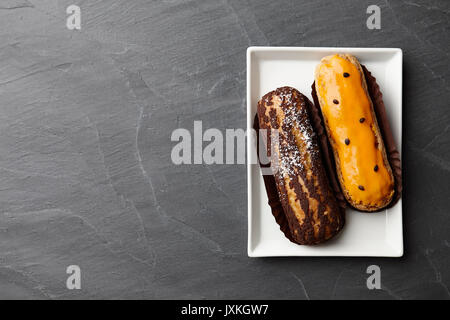 Weiße Platte mit verschiedenen französischen eclairs auf Stein Hintergrund, Ansicht von oben Stockfoto