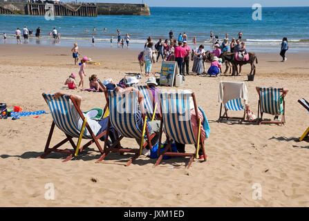 Im Sommer saßen Besucher Touristen auf Liegestühlen am Strand von South Bay Scarborough North Yorkshire England Großbritannien Stockfoto