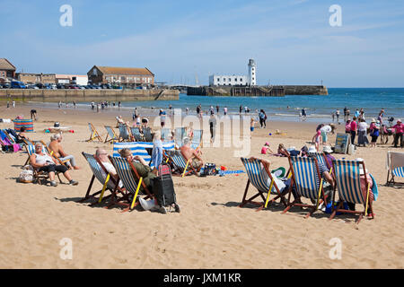 Menschen Besucher Touristen saßen auf Liegestühlen am South Bay Strand im Sommer Scarborough North Yorkshire England Großbritannien GB Großbritannien Stockfoto