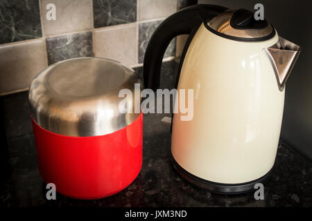 Cremefarbene Wasserkocher mit einem roten und Edelstahl Kaffee Kanister. Grauen und weißen Fliesen im Hintergrund Stockfoto