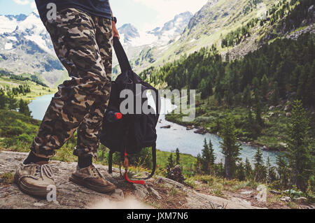 Travel Concept: Trekker mit touristischen Sticks und Rucksack auf See. Touristen Backpacker hält den Rucksack in der Hand auf dem Hintergrund des schönen Doppelzi. Stockfoto